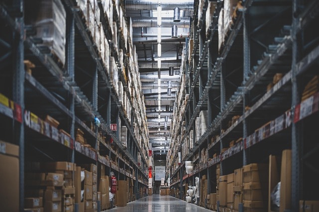 Warehouse aisle with tall racks of boxed stock, illustrating supply and inventory risks covered by AI scenario analysis