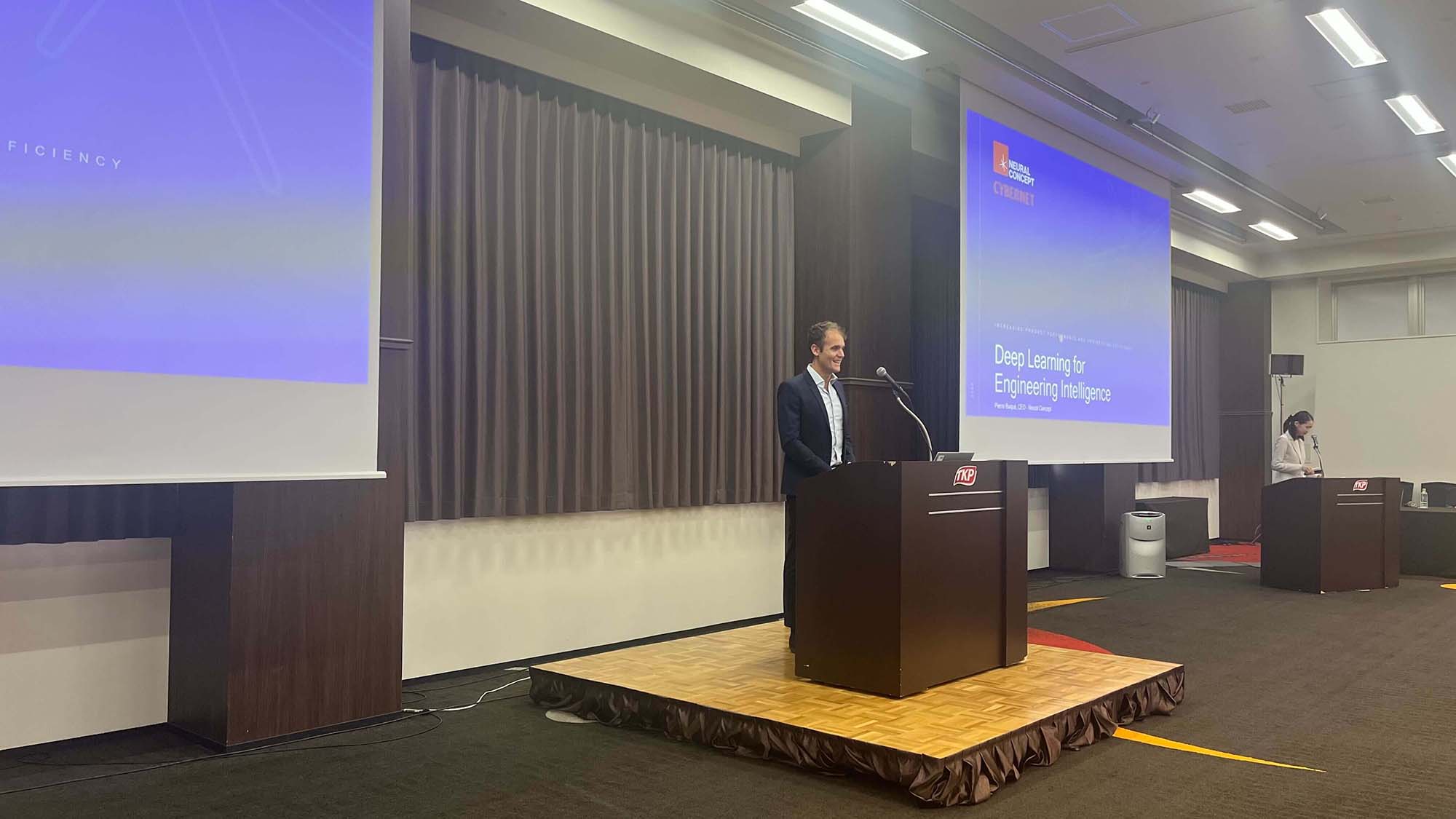 Speaker at a podium at the Cybernet seminar in Tokyo, slide titled Deep Learning for Engineering Intelligence