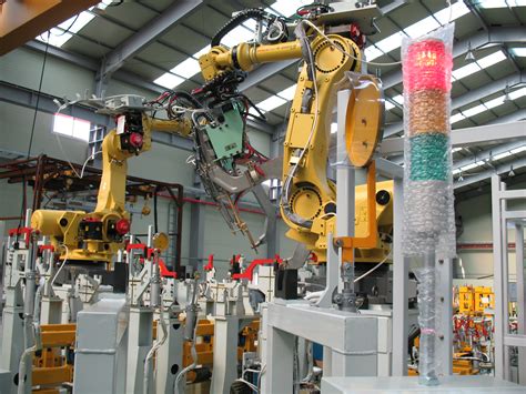 Yellow industrial robot arms in a manufacturing cell with part fixtures and a stack signal light