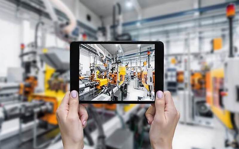 Tablet held up to a factory floor showing a live digital view of the production equipment, the factory of the future