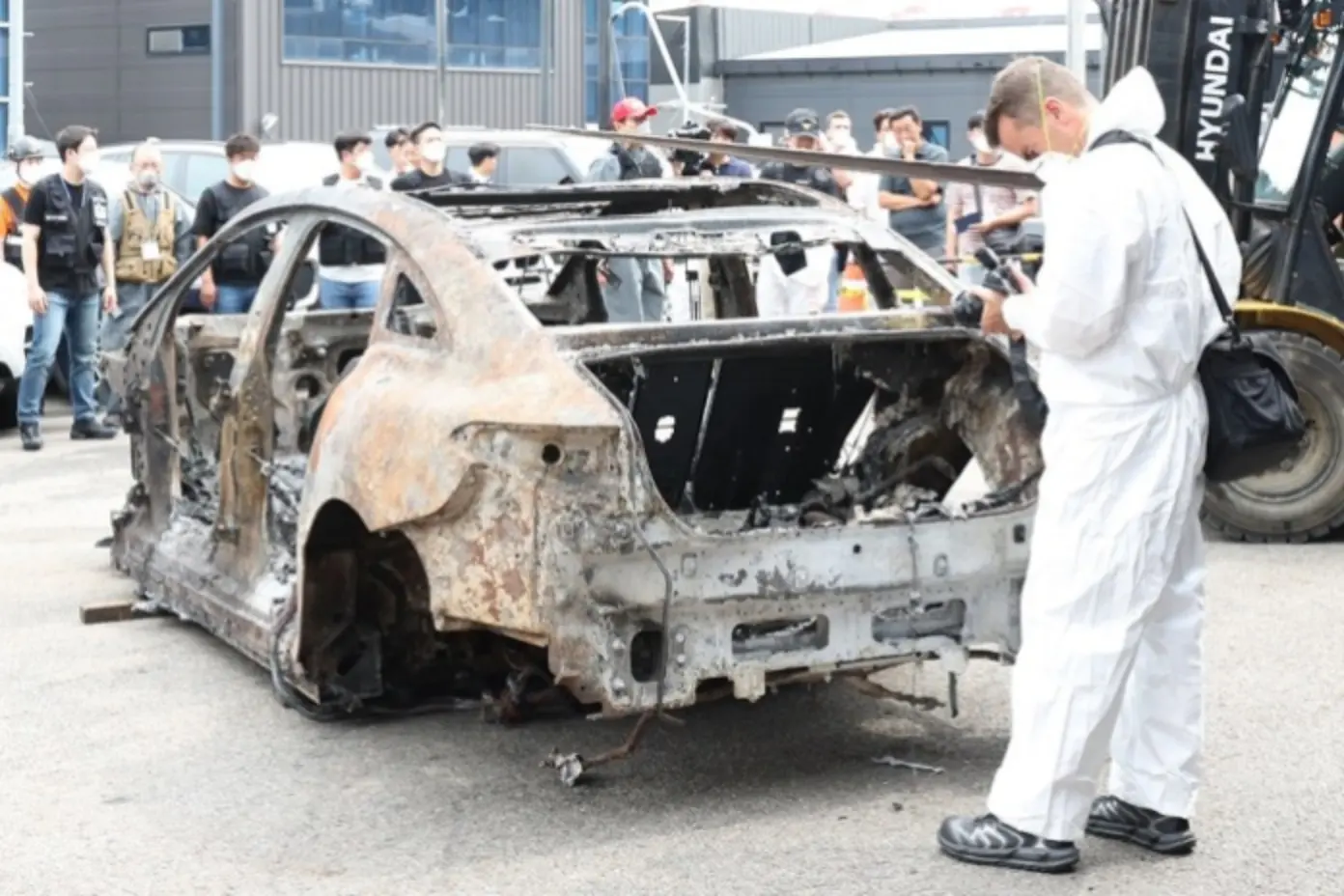 Investigator in protective suit examining a burnt-out electric car, showing why EV batteries need advanced thermal management