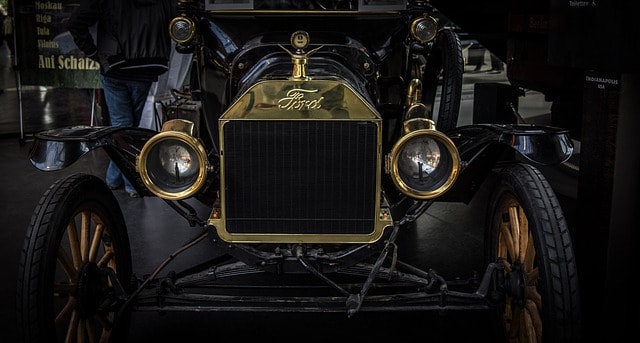 Front of an early Ford Model T with brass radiator and headlamps, emblem of Henry Ford's assembly-line mass production