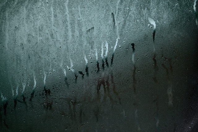 Condensation droplets running down a fogged car window, showing why cabin AC dehumidification matters